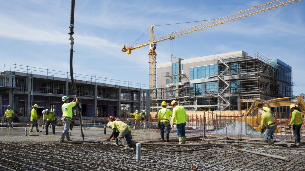 Commercial construction project in Jacksonville Florida with concrete placement crews, tower crane operations, reinforced slab work, and active building development